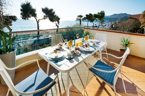 Een eettafel op een balkon met uitzicht op zee en heuvels.