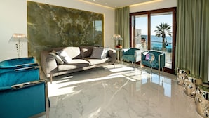 A modern living room with a marble floor, a large abstract wall art, a sofa, a teal armchair, and a view of the ocean through large windows.
