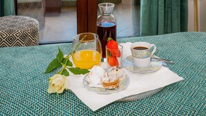 A balcony with a table set for breakfast, including a fruit bowl, a glass of orange juice, a cup of coffee, and pastries.
