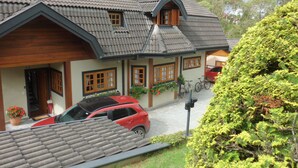 Une maison avec un toit en pente, des fenêtres en bois et une voiture rouge garée dans l’allée.