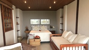 Une chambre à coucher avec un lit, deux tables de chevet, un banc en bois, un panier en osier rempli de pommes et une fenêtre donnant sur des arbres.