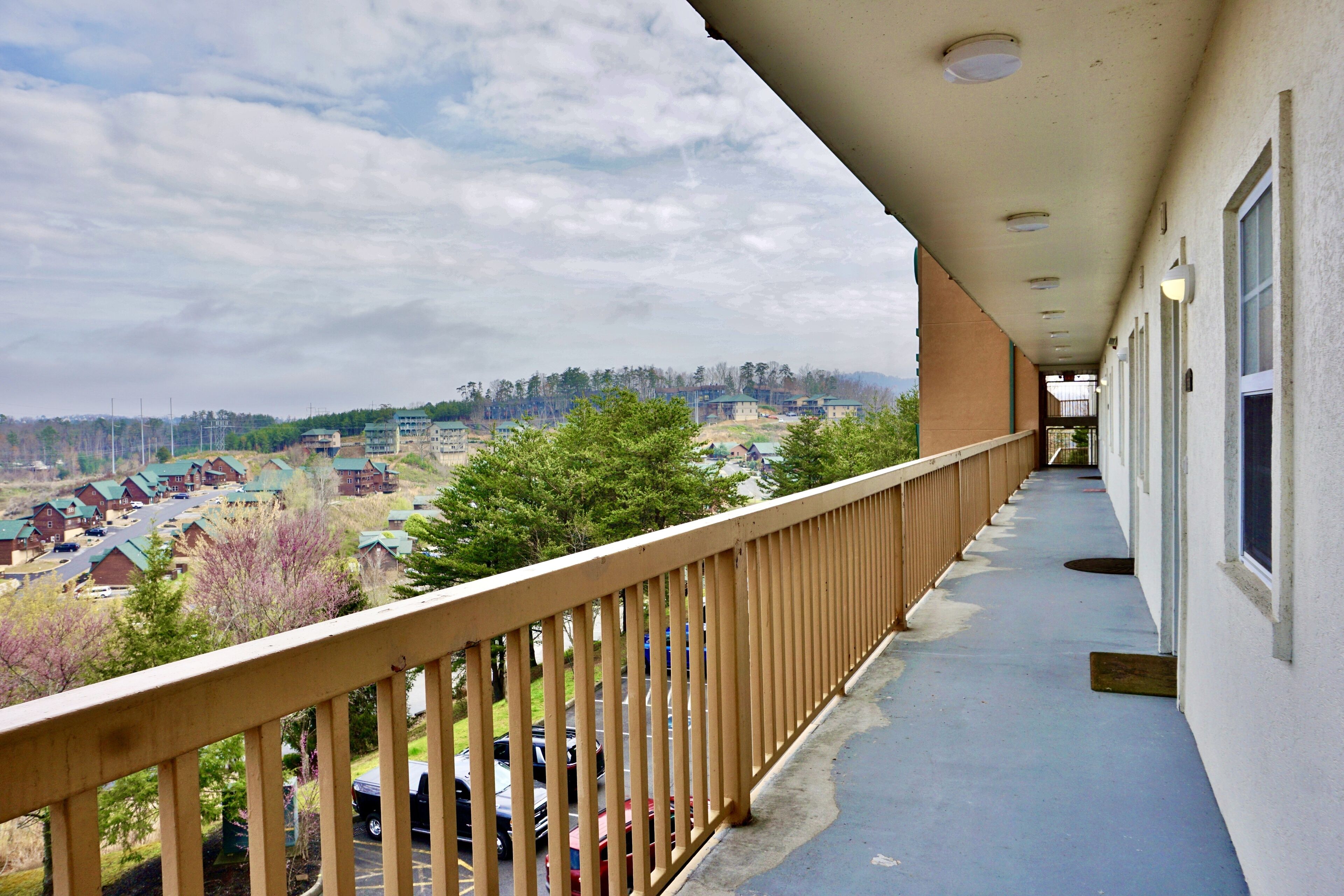 Un balcon donnant sur un quartier résidentiel, avec une balustrade en bois et un immeuble doté de fenêtres.