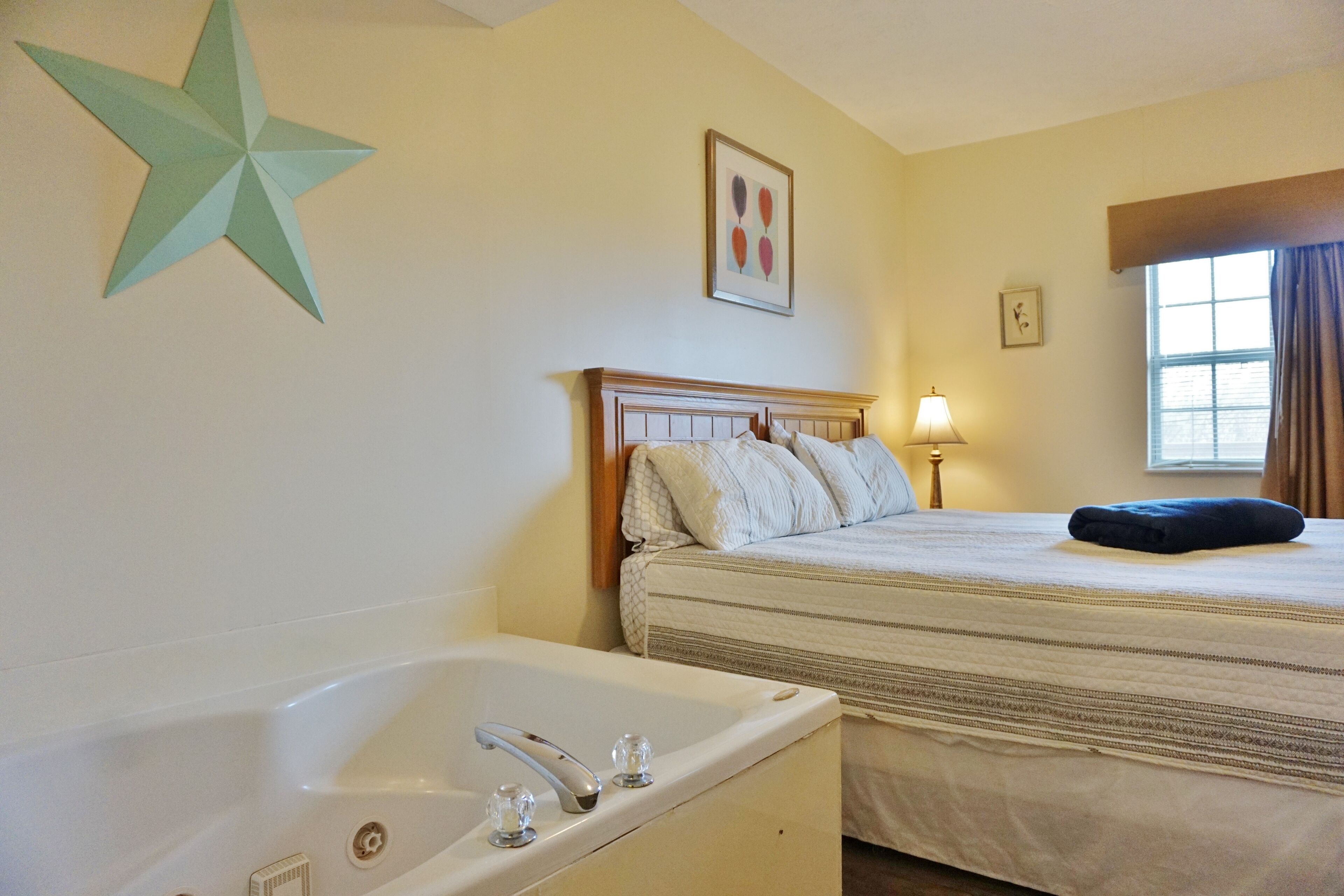 Habitación de hotel con cama, adorno de estrella en la pared, un cuadro enmarcado, una ventana con cortinas y una bañera.