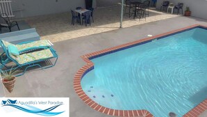 Une piscine dont le bord est revêtu de carrelage, entourée d’un patio aménagé avec des meubles d’extérieur et un espace salon abrité.