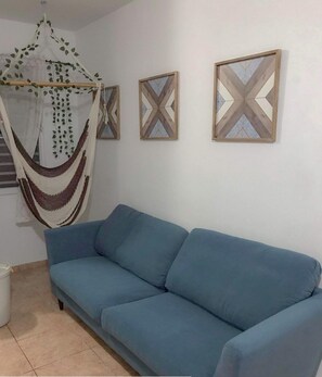 A room with a blue sofa, a hanging hammock, and three framed geometric wall art pieces.