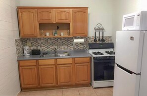 A compact kitchen with wooden cabinets, a gas stove, a microwave, and a refrigerator.