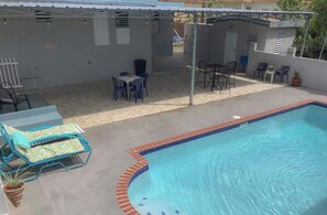 A swimming pool with a tiled edge, surrounded by a patio area with outdoor furniture and a covered seating area.