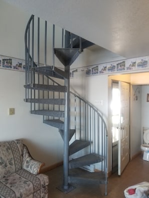 Cozy living space with a spiral staircase, patterned sofa, and framed coastal artwork.