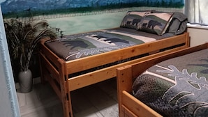 Uma cama de madeira com um mural de paisagem montanhosa, um travesseiro com desenho de urso e um vaso de planta.