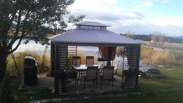 Um gazebo com mesa e cadeiras, cercado por paisagem natural e um corpo d'água.