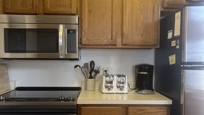 Une cuisine avec des meubles de rangement en bois, un four à micro-ondes en acier inoxydable, un grille-pain et une machine à café.