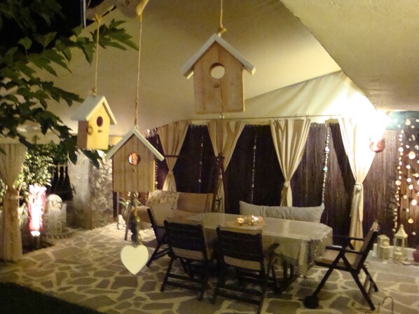An outdoor dining area with stone flooring, a table, chairs, and hanging birdhouse decorations.
