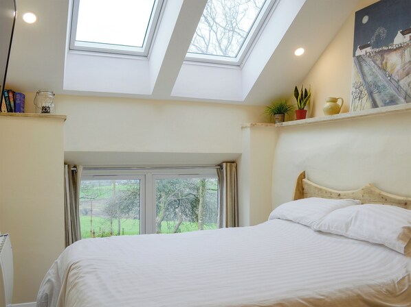 Une chambre avec une lucarne, un lit, une fenêtre et un tableau accroché au mur.