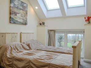 A bedroom with a large bed, skylights, a painting, and a view of greenery outside.