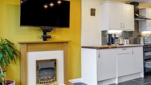 A modern kitchen with a flat-screen TV, a built-in fireplace, white cabinets, and a stove. - Dutch Barn One - UK12872 (Ymwlch, near Porthmadog)