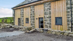 A stone and wooden building with multiple windows, a stone wall foundation, and a gravel driveway. - Dutch Barn One - UK12872 (Ymwlch, near Porthmadog)