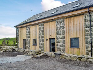 Un bâtiment en pierre et en bois, doté de nombreuses fenêtres, avec des fondations en pierre et une allée gravillonnée.