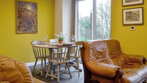 A dining area with a table set for two, two chairs, a potted plant, and a window with a view of trees. - Dutch Barn One - UK12872 (Ymwlch, near Porthmadog)