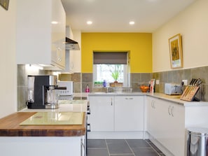 A modern kitchen with white cabinets, a coffee machine, a toaster, and a window with a view of greenery.