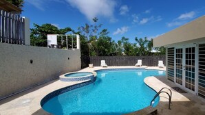 A swimming pool with a tiled edge, surrounded by a concrete deck and a wooden fence. - Paradise Haven in Palmas del Mar, a charming house for the perfect vacations! (Humacao)