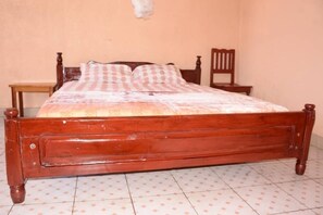 A wooden bed with a checkered bedspread in a room with a tiled floor and plain walls. - Eden Condo Hotel (Muhoza)