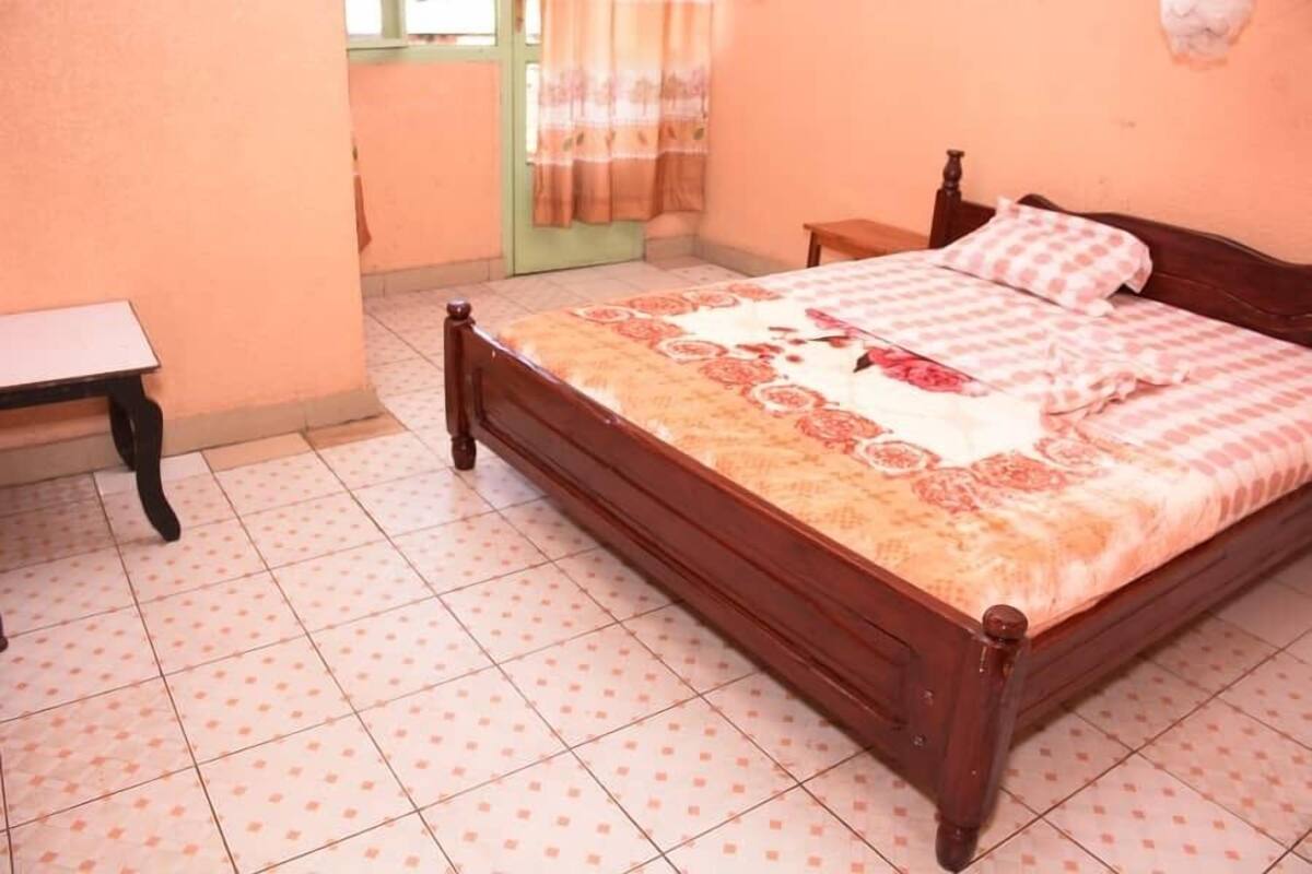 Een slaapkamer met een houten bed, een nachtkastje en een raam met gordijnen.