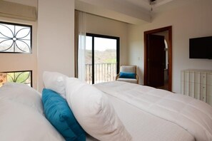 A bedroom with a large bed, a chair, a TV, and a balcony with a view of the outdoors.
