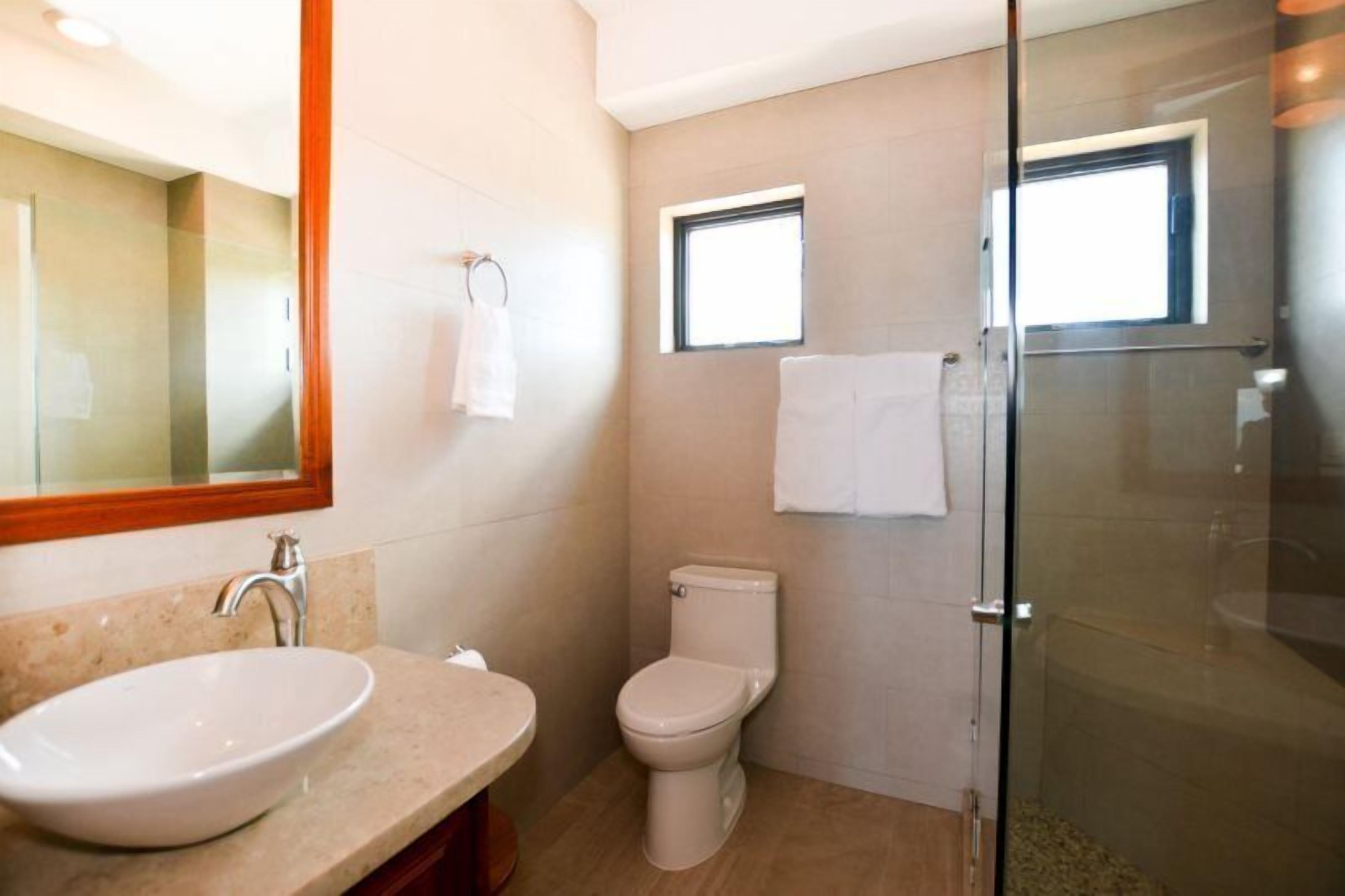 Een moderne badkamer met een douche met glazen wand, een wit wastafelmeubel en een toilet.