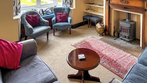 Una sala de estar acogedora con un sofá, dos sillones, un televisor, una chimenea y vistas al jardín.