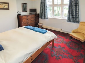 A bedroom with a bed, a dresser, a chair, a television, and a window with curtains. - What more could you ask for than a spacious family home in a rural haven. (Yanwath, near Penrith)