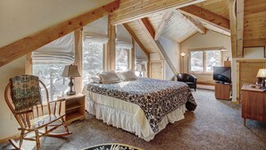 Une chambre confortable située dans les combles, avec un grand lit, un fauteuil à bascule, un bureau et un téléviseur.