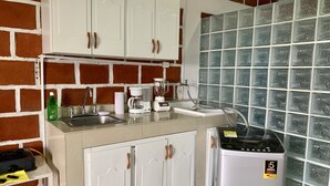 Cozinha compacta com armários brancos, cafeteira, liquidificador e um pequeno frigorífico.