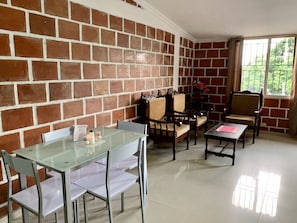 A dining area with a glass table and chairs, a brick wall, and a view through a window. - Loft Two (Cali)
