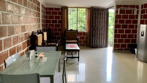 Cozinha com parede de tijolos, mesa de jantar com cadeiras, geladeira e janela com vista para áreas verdes.
