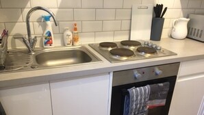 Eine Küche mit Spüle, Herd und Backofen. Auf der Arbeitsfläche stehen Reinigungsmittel.