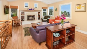 A spacious living room with a fireplace, leather sofas, wooden furniture, and large windows. - Sunny Beach Cottage with Amazing Views (Stinson Beach)