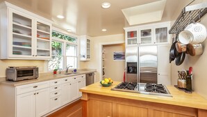 A modern kitchen with white cabinetry, a central island, and stainless steel appliances. - Sunny Beach Cottage with Amazing Views (Stinson Beach)