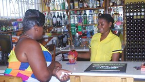 A bar with a counter, shelves with bottles, and a menu. - Global Villa Hotel (Lucea)