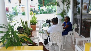 A seating area with white chairs and tables, surrounded by potted plants. - Global Villa Hotel (Lucea)