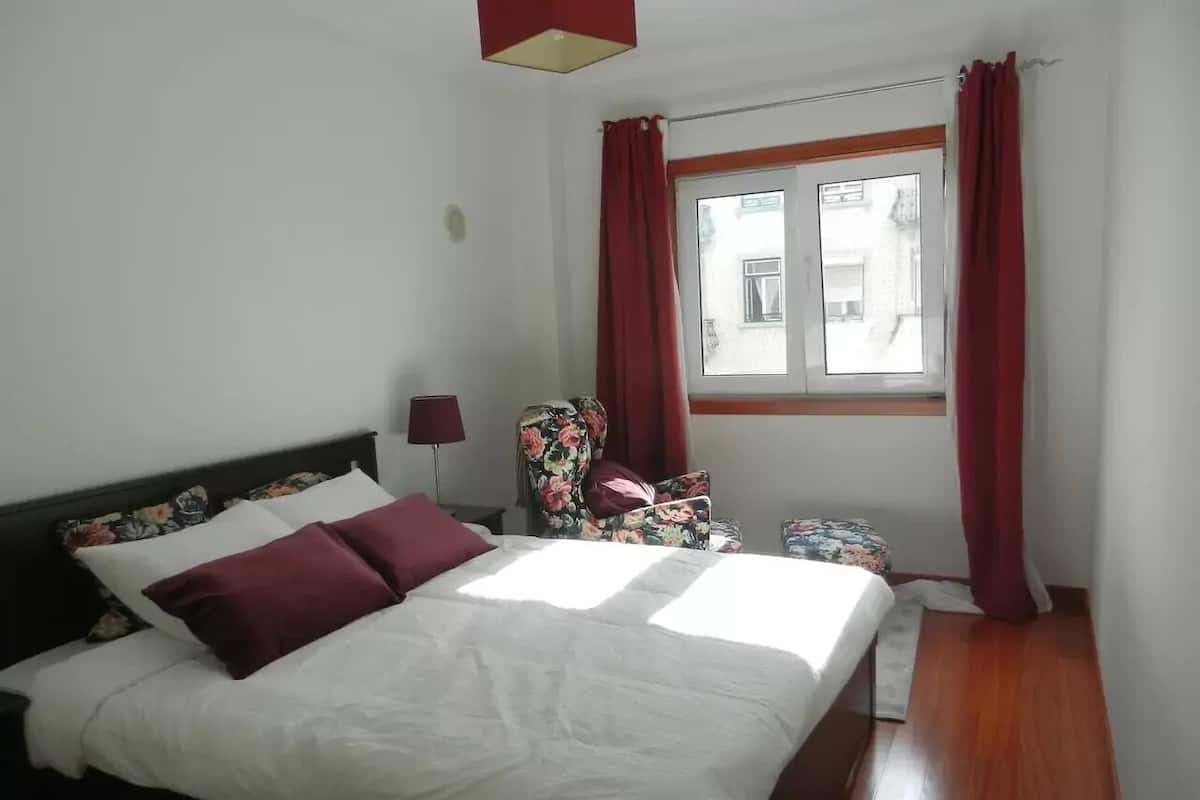 Un dormitorio con cama, una silla, una ventana y una lámpara.