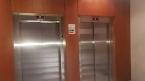 Dos puertas de ascensor metálicas con una pantalla digital encima de cada una, y un letrero de seguridad en la pared.