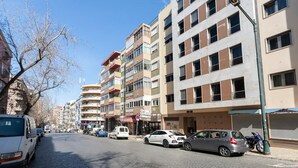Un edificio de varios pisos con espacios residenciales y comerciales, que presenta diversas tiendas y automóviles estacionados en la calle.