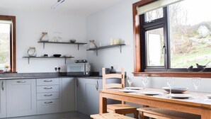 A modern kitchen with grey cabinets, a wooden dining table, and a window with a view of the outdoors.