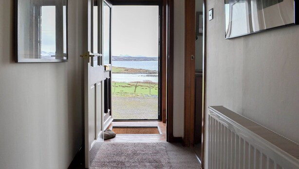 A hallway leading to a door with a view of a beach and sea.