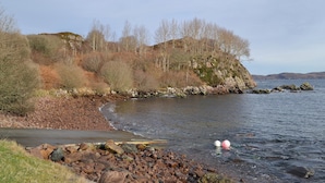 A coastal landscape with rocky shores, a clear sky, and sparse vegetation.