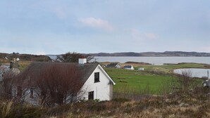 A white house with a sloped roof, surrounded by a grassy field and a body of water.