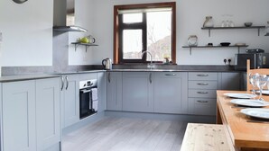 A modern kitchen with grey cabinets, a built-in oven, a window with a view, and a dining area with a wooden table set for two.
