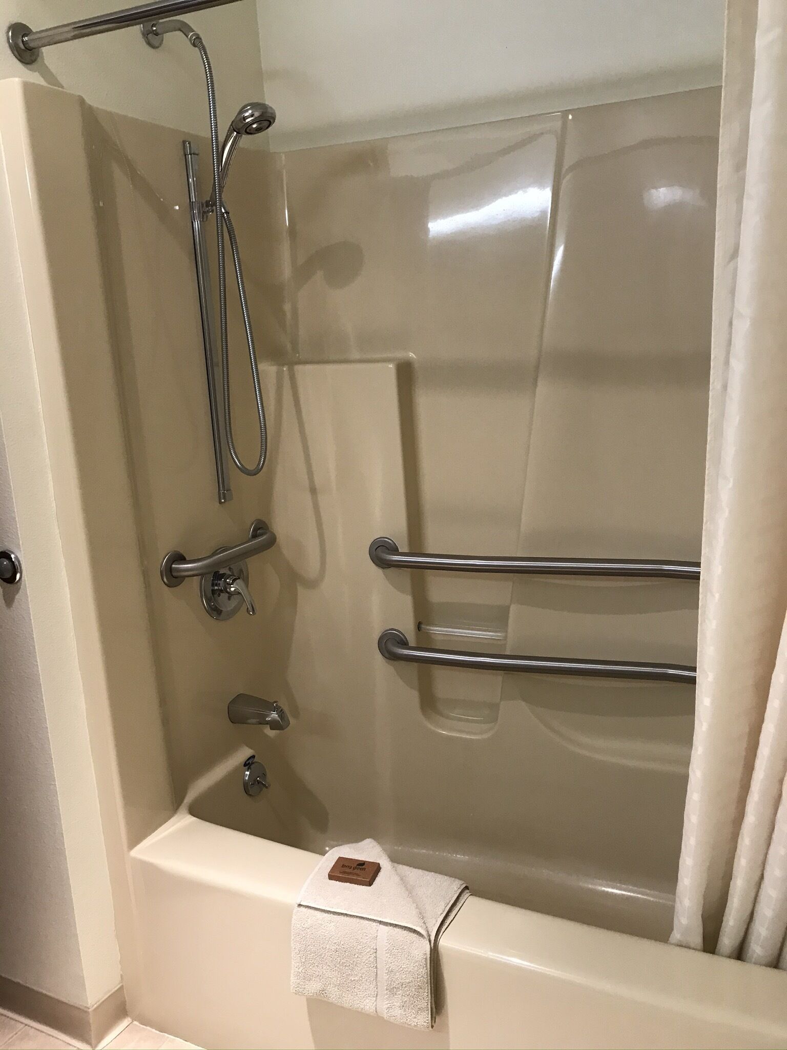 Un baño moderno con ducha envuelta en vidrio, barras de apoyo y un perchero.