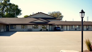 A motel with a large parking lot, a central entrance, and a row of rooms with windows. - Dutch Country Inn (Kalona)