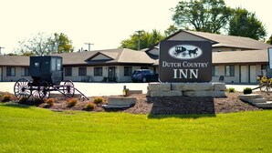 A Dutch Country Inn with a signboard, a horse-drawn carriage, and a building with a sloped roof. - Dutch Country Inn (Kalona)